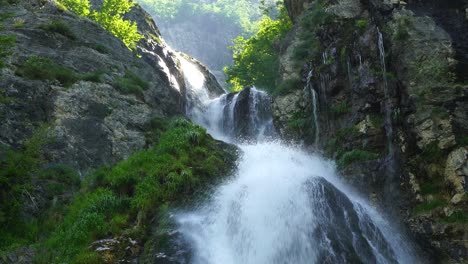 Sunrise-on-high-mountains-of-Albanian-Alps,-waterfall-scenery-with-rocky-slope-and-green-trees