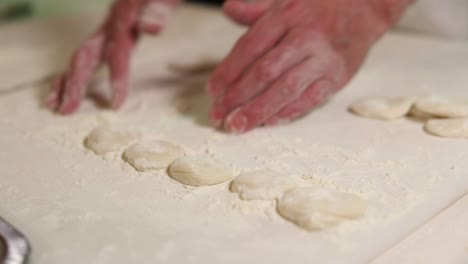 Chef-flattens-a-ball-of-dough-using-his-palms-on-a-floured-countertop