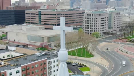 Aerial-view-around-a-church-cross,-with-city-street-background---circling,-drone-shot