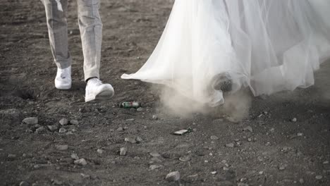 Unusual-retro-styled-wedding-couple-in-sneaker-and-boots-walking-over-grey-stones-stiring-up-dust-and-dirt---cinematic-low-slowmotion-shot