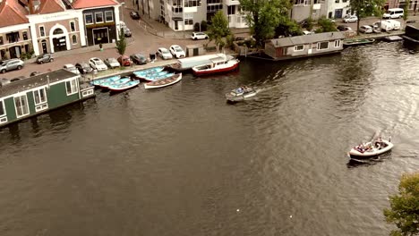 Haarlem-canal-with-boats-passing-by-moored-Houseboats,-Netherlands---Aerial