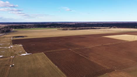 Plowed-fields-in-vast-countryside-on-clear-day,-aerial-drone-shot