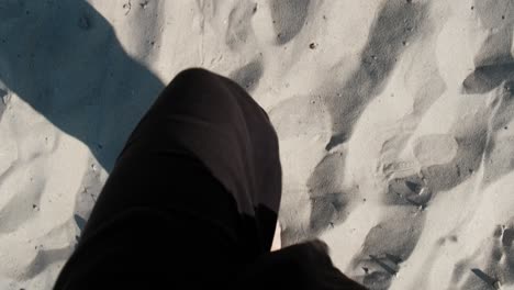 Bare-feet-of-woman-in-black-pants-walking-on-sand