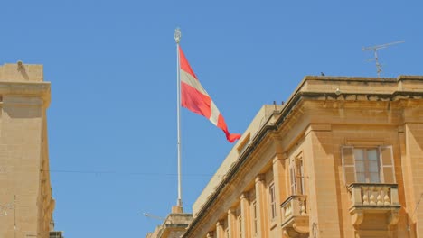 The-Flag-of-the-Knights-Of-St-John-flies-proudly-above-the-buildings-of-Malta---Its-red-and-white-cross-a-strong-contrast-to-the-blue-sky-above