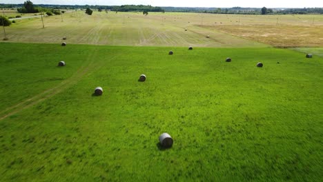 Aerial-view-hay-bales-in-the-green-agriculture-field,-bailed-hay-drying-on-ranch-land,-the-straw-is-compressed-into-roles,-sunny-summer-day,-wide-drone-shot-moving-forward
