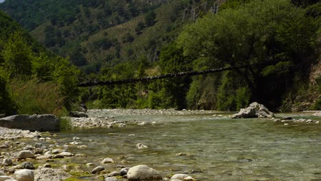 Footbridge-hanging-over-river-stream,-lush-vegetation-on-high-mountains-in-Albania