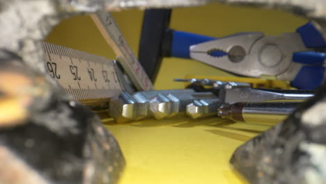 Close-up-dolly-shot-showing-tools-for-work,-measuring-stock,screwdriver-and-hammer-on-yellow-surface