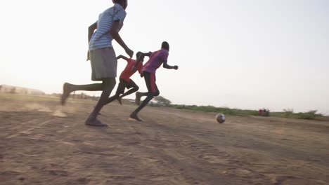 Mehrere-Schwarze-Jungen-Spielen-Draußen-Auf-Einer-Unbefestigten-Ebene-Fußball