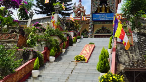 Vista-Ascendente-Desde-Las-Escaleras-Del-Templo-Budista-De-Entrada-De-Giac-Nguyen-Con-Banderas-Típicas-Y-Plantas-Ornamentales