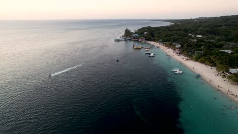 Aerial-view-of-the-coast,-boats,-green-palms-on-the-sandy-beach-at-sunset