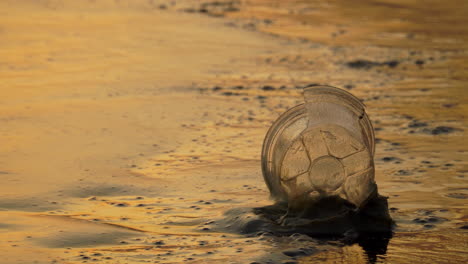 Closeup-shot-of-an-empty-plastic-cup-laying-on-the-beach-as-the-water-splashes-up-against-it-in-the-late-afternoon