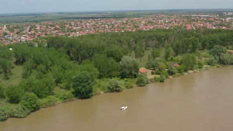 Aerial:-boat-travelling-along-murky-river-in-Serbian-city