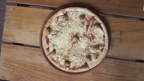 Rotating-margarita-pizza-with-cheese-and-olives-on-wooden-table,close-up-top-down