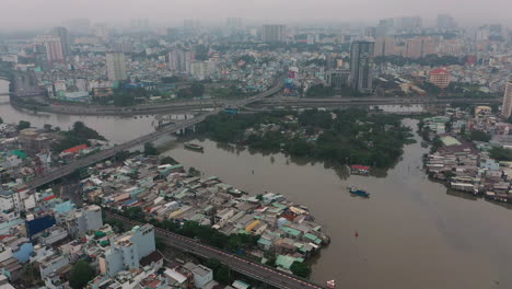 Foggy,smoggy-early-morning-drone-footage-flying-in-towards-the-junction-of-major-canals-with-working-boats,-road-systems,-bridges-in-Saigon,-Ho-Chi-Minh-City,-Vietnam