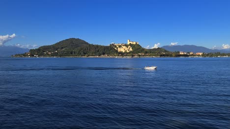 Small-motorboat-navigating-in-calm-lake-waters-of-Maggiore-lake-in-Italy-with-Angera-castle-in-background