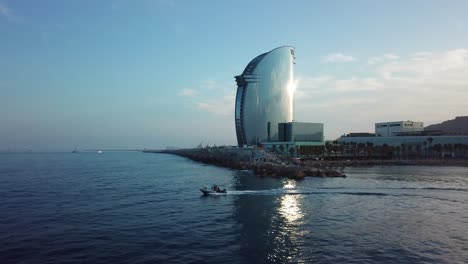 Motorboot,-Das-über-Das-Mittelmeer-In-Barcelona-Spanien-Mit-W-Barcelona-Hotel-Im-Hintergrund-Beschleunigt