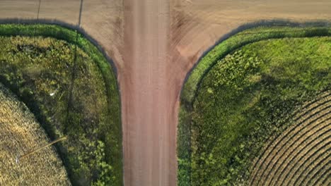 Vertical-aerial-shot-in-4k-showing-slow-forward-movement-over-red-dirt-road-intersection-between-wheat-and-barley-fields-in-rural-Canada