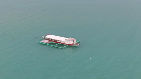 Beautiful-aerial-view-orbiting-the-fishing-boat-stop-and-floating-in-calm-turquoise-seawater-not-far-away-from-the-shore