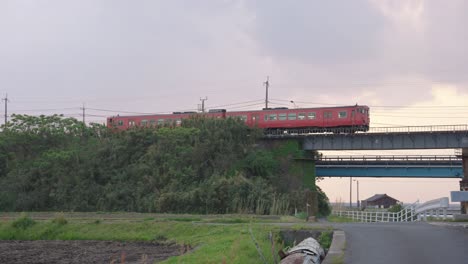 Red-countryside-local-train-crossing-bridge-in-Mikuriya,-Tottori-Japan
