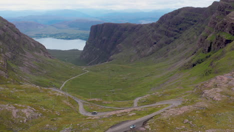 Rotating-drone-shot-of-vehicles-on-Bealach-Na-Ba-Applecross-road-through-the-mountains-of-the-Applecross-peninsula,-in-Wester-Ross-in-the-Scottish-Highlands