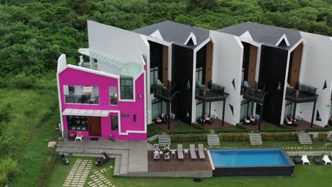 Aerial-ascending-shot,-tourists-relaxing-on-outdoor-chairs-in-front-of-beautiful-modern-accommodation-next-to-swimming-pool-on-a-idyllic-day-at-Xiaoliuqiu-Lambai-Island,-Pingtung-county,-Taiwan