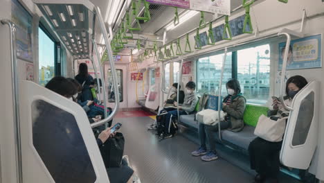 People-Wearing-Face-Masks,-Using-Smartphone-And-Sitting-In-The-Train-In-Tokyo,-Japan---wide-shot