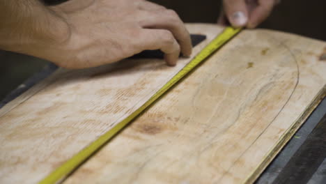 Hand-of-craftsman-working-on-wooden-skateboard-with-yellow-measure-tape