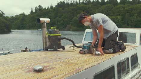 Young-man-belt-sanding-planks-on-wooden-boat-forecabin