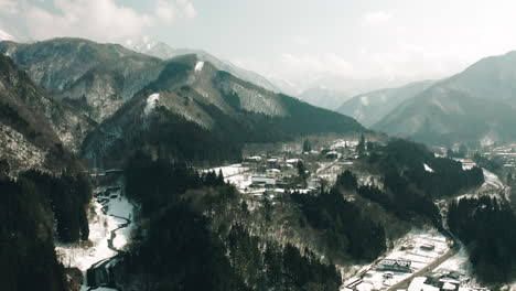 Drone-shot-of-snow-covered-village-by-the-mountains-in-Japanese-countryside-of-Okuhida,-Gifu-during-daytime