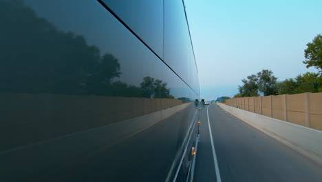 Side-view-of-a-public-bus,-shuttle,-or-school-bus-driving-and-the-road-reflection-on-it