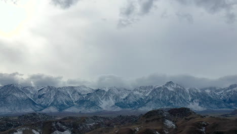Cloudscape-rolling-over-snowy-mountain-range,-aerial-drone-view