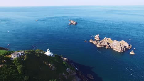 View-from-above-of-a-pretty-white-lighthouse-on-the-rocky-shoreline-of-the-idyllic-landscape-of-Sark-Island,-southwestern-English-Channel