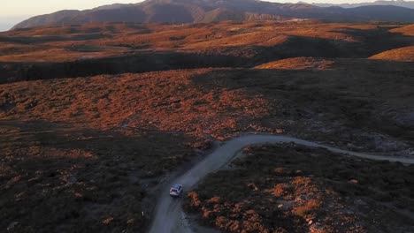 A-solitary-car-drives-across-the-Denniston-Plateau-in-New-Zealand,-the-camera-tilts-up-from-the-car-to-reveal-the-great-plateau