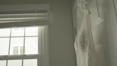 Tight-Shot-of-a-Wedding-Dress-Hanging-Next-to-a-Window-in-Bridal-Suite