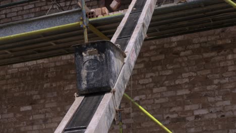 Bricklayer-Sends-Mortar-Bucket-Up-Elevator-Conveyor-Belt,-SLOW-MOTION