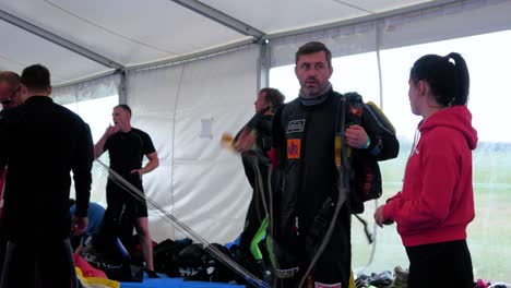 Professional-caucasian-male-skydiver-unstrapping-his-parachute-after-a-successful-jump-and-preparing-it-for-next-jump,-medium-handheld-shot