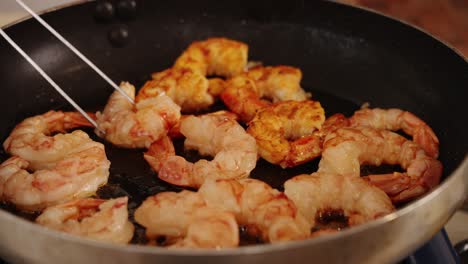 Close-up-shot-of-tasty-fresh-prawns-browning-in-a-saute-pan-in-slow-motion,-with-chef-using-tongs-to-flip-the-prawns