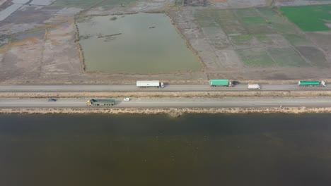 Luftaufnahme-Von-Lastwagen-Und-Tanklastwagen,-Die-Entlang-Der-Straße-An-Landwirtschaftlichen-Flächen-In-Sindh-Vorbeifahren