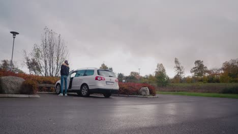 Young-Tall-Man-With-Cap-Enters-His-White-Car-and-Drives-Away,-Static-Wide-Shot