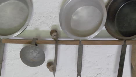 Close-up-pan-shot-of-old-medieval-pans-hanging-on-wooden-construction-in-old-house---Wall-in-old-cuisine-with-antique-furniture-and-tools