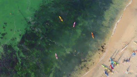 Shoal-of-surfers-coral-reef-riding-at-Marazion-UK-aerial