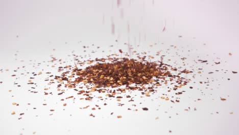 Close-Up-Of-Chili-Red-Pepper-Flakes-Falling-Into-Pile-Onto-Surface