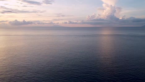 Aerial-drone-of-beautiful,-peaceful-and-relaxing-pink-and-blue-sunset-hues-over-rippled-ocean-on-remote,-secluded-tropical-island