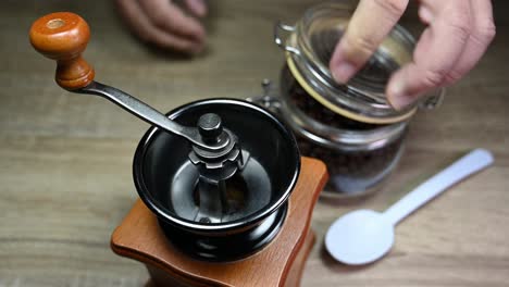 Hands-opening-a-jar,-uses-a-white-spoon-to-bring-beans-into-the-grinder-and-returns-the-spoon-on-the-table