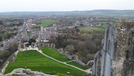 Aerial-drone-flview-over-Corfe-Castle-ruins-perched-on-hill-and-green-English-countryside,-UK