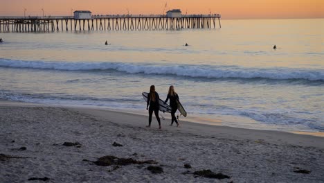 Zwei-Surfermädchen,-Die-Kurz-Nach-Sonnenuntergang-Am-Strand-Spazieren-Gehen