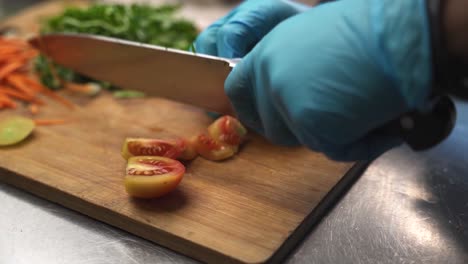 Chef-cutting-tomatoes-alongside-other-vegetables-on-kitchen-cutting-board
