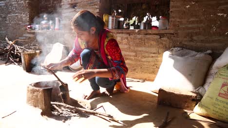 Authentic-real-rural-life-scene-of-poor-Indian-Dalit-woman-light-fire-for-cooking-outdoor-blowing-on-wooden-sticks
