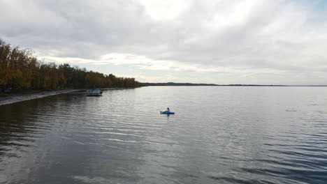 Person-sitting-in-a-blue-kayak,-paddling-slowly-along-the-shoreline-of-buffalo-lake,-Alberta