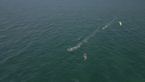 One-kite-surfer-quickly-follows-another-in-green-open-water-aerial